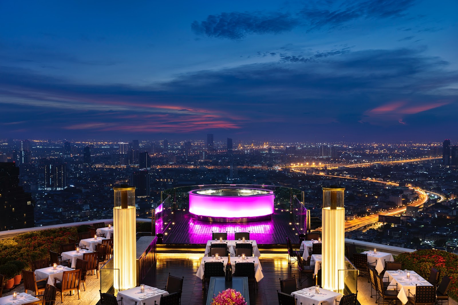 Sirocco's outdoor terrace at dusk with a lit bar and the city stretching to the horizon