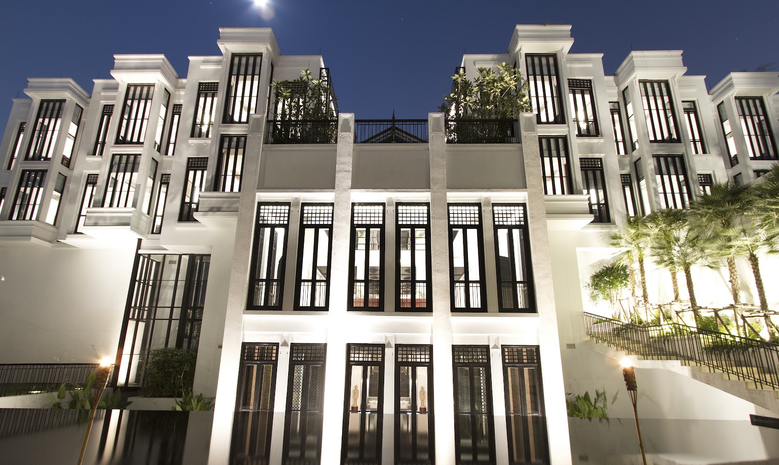 The white and black facade of The Siam hotel lit at night