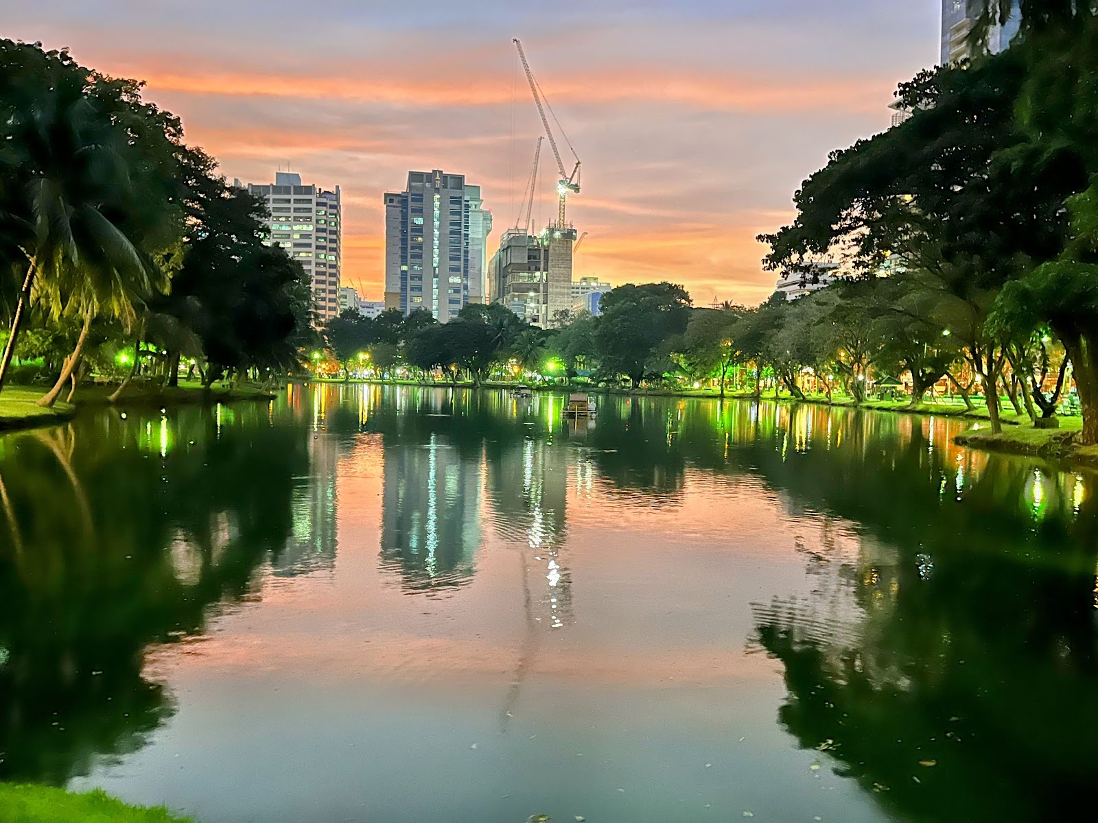 Sunset sky reflected in the lake at Lumphini Park with city towers behind