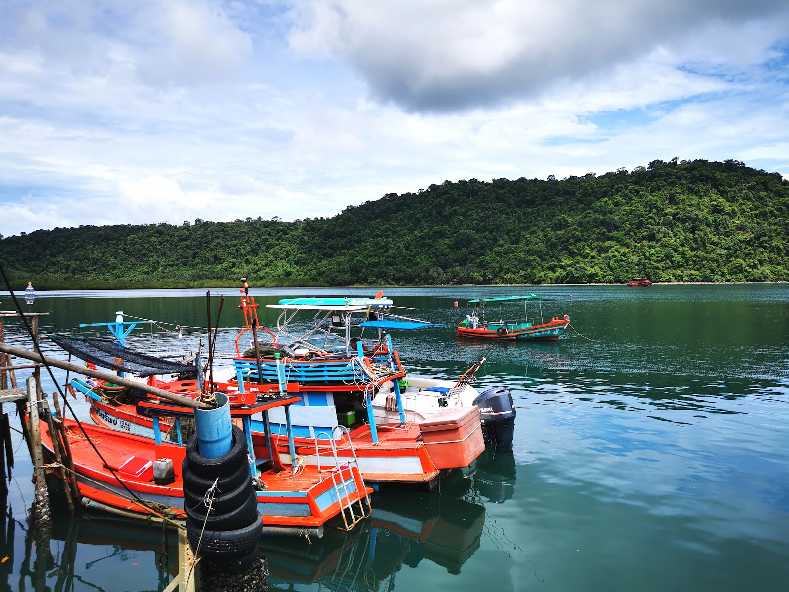 Colorful wooden fishing boats moored at Ao Salad pier on Koh Kood, with forested hills behind