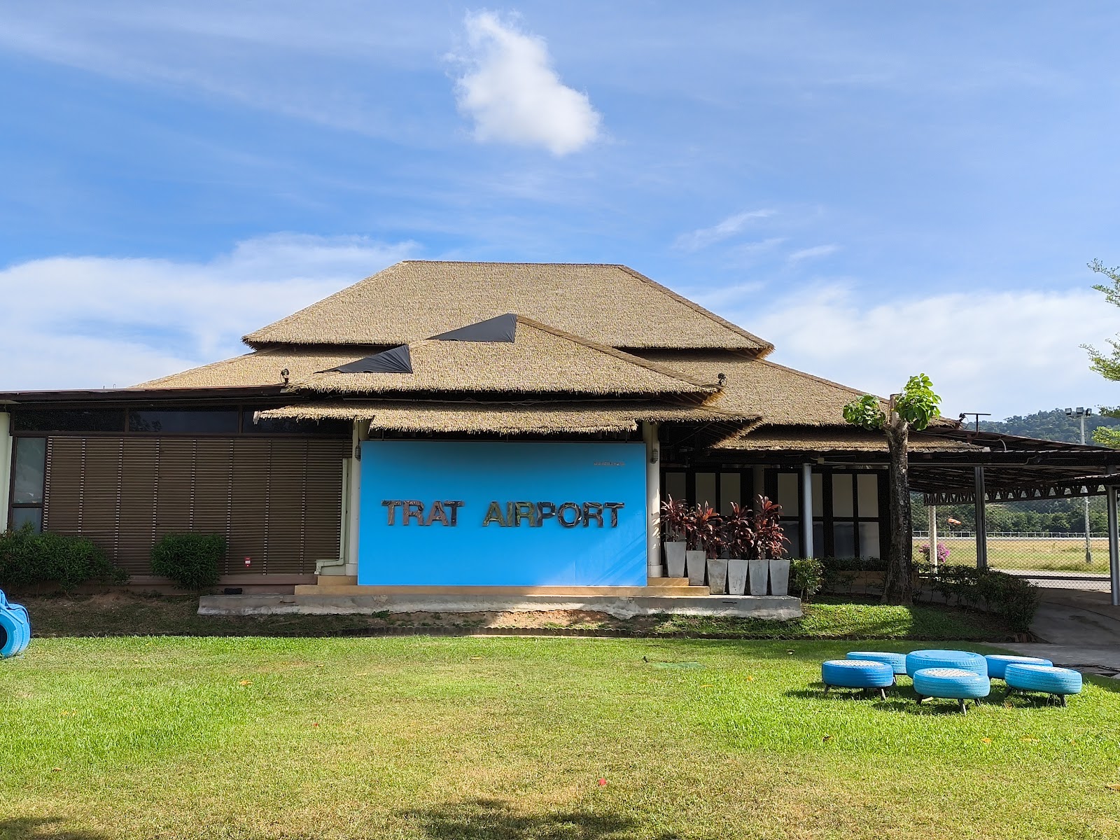 The low thatched terminal building of Trat Airport with its blue airport sign