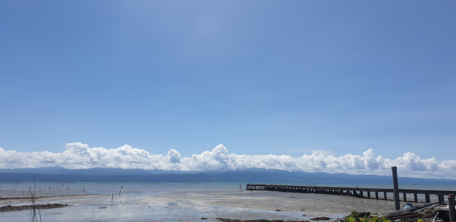The long jetty of Laem Sok pier stretching out over shallow water under a blue sky