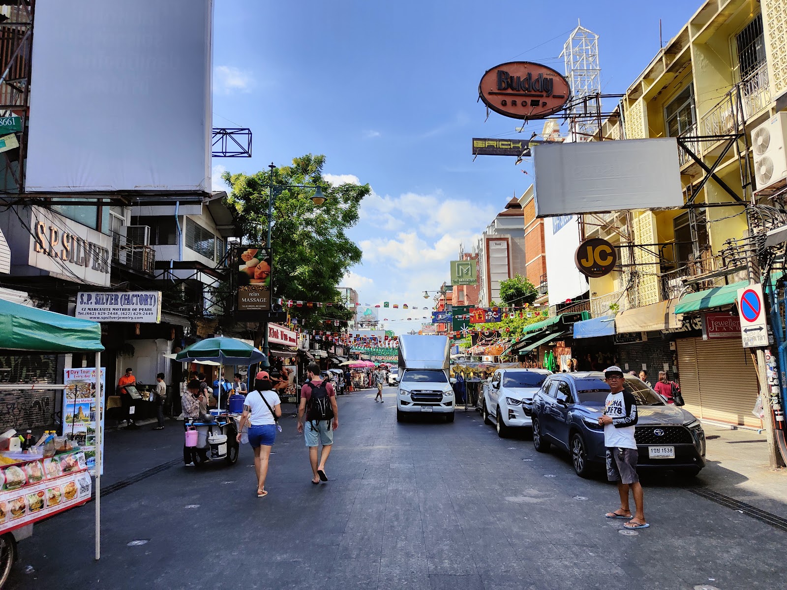 Khao San Road in daylight, lined with shophouses, signs and street stalls