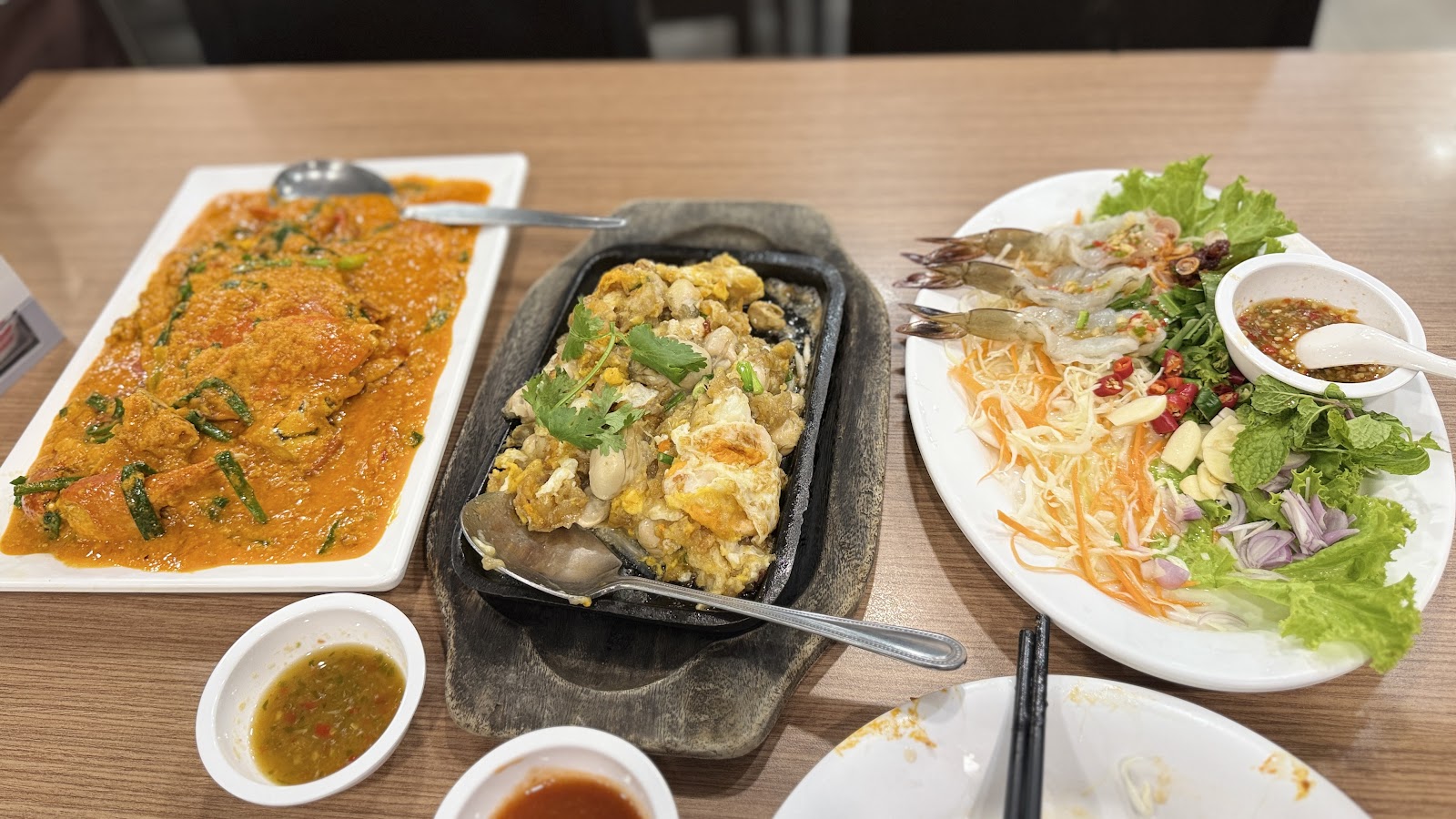 Curry crab, stir-fried dishes and small bowls of dipping sauce on a table at Somboon Seafood
