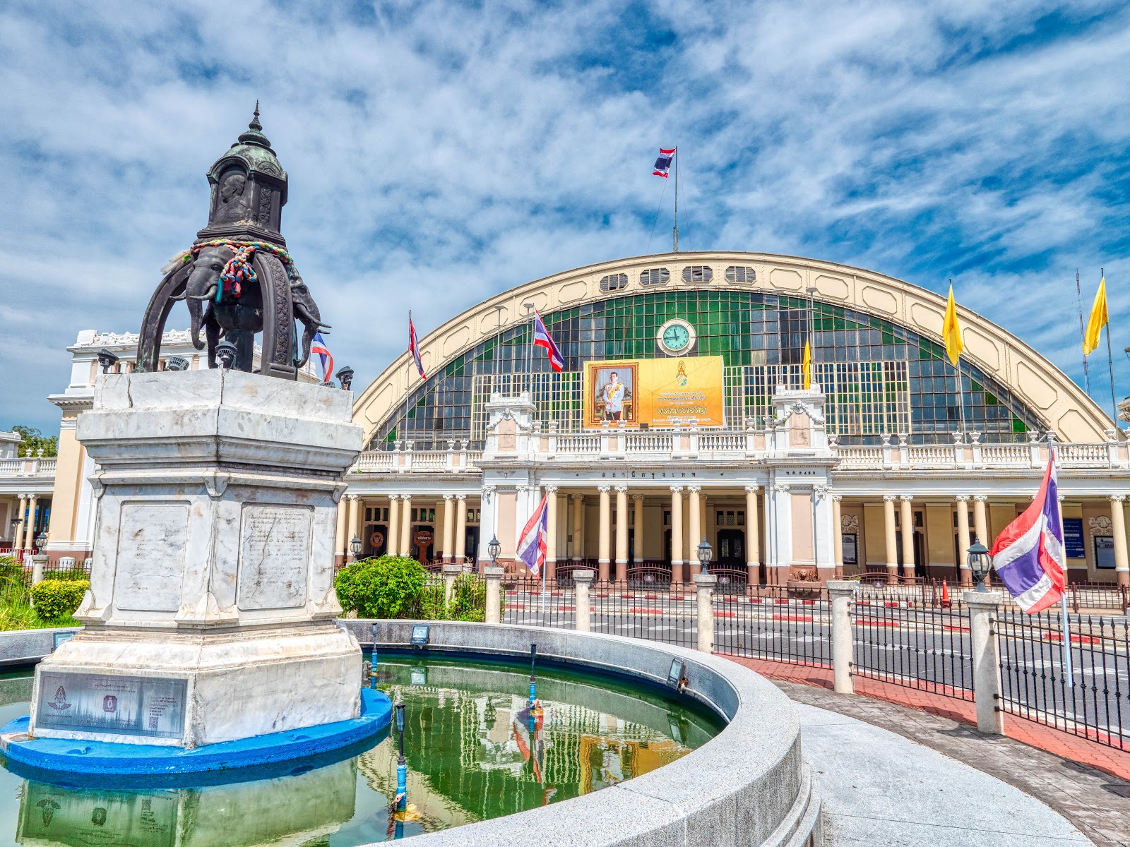 The arched facade of Hua Lamphong station behind a fountain and monument