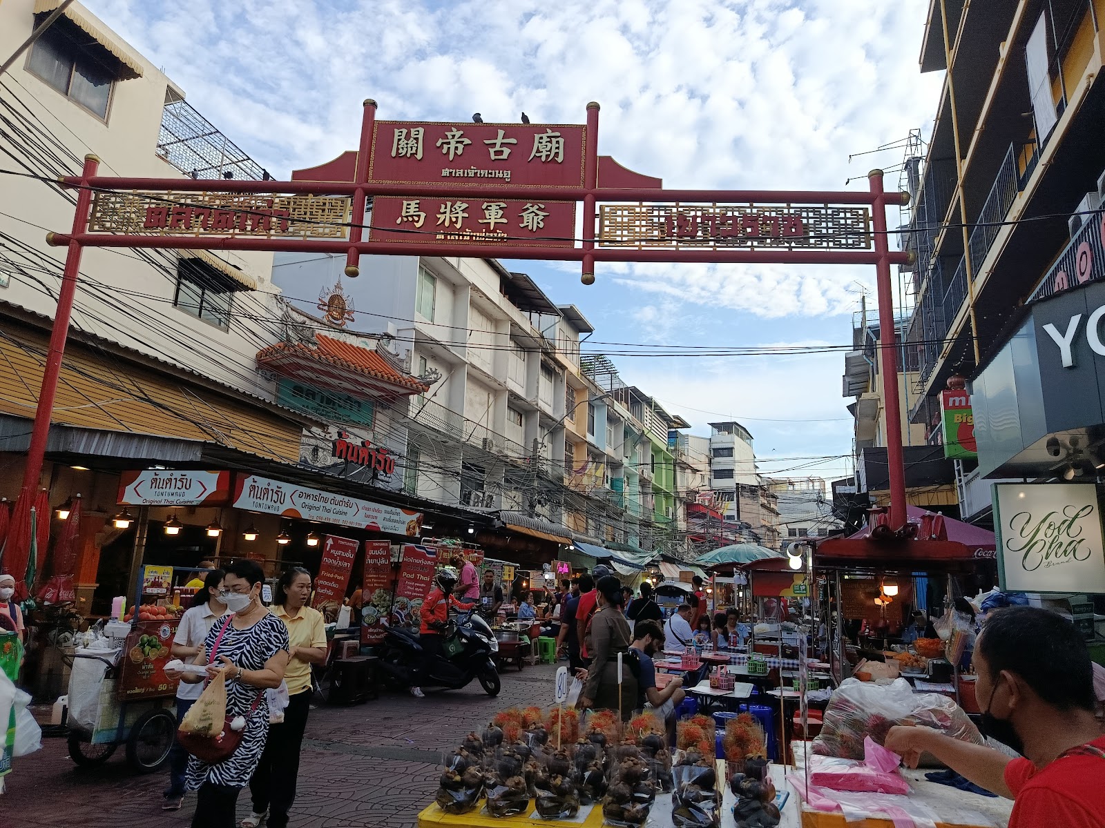 Street-food stalls under a red Chinese gateway on a street in Bangkok's Chinatown