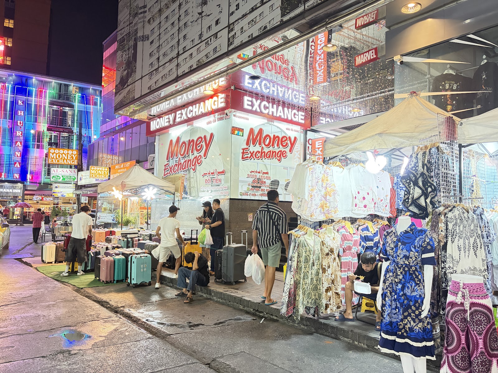 Clothing stalls and luggage on the pavement at Pratunam Market in the evening