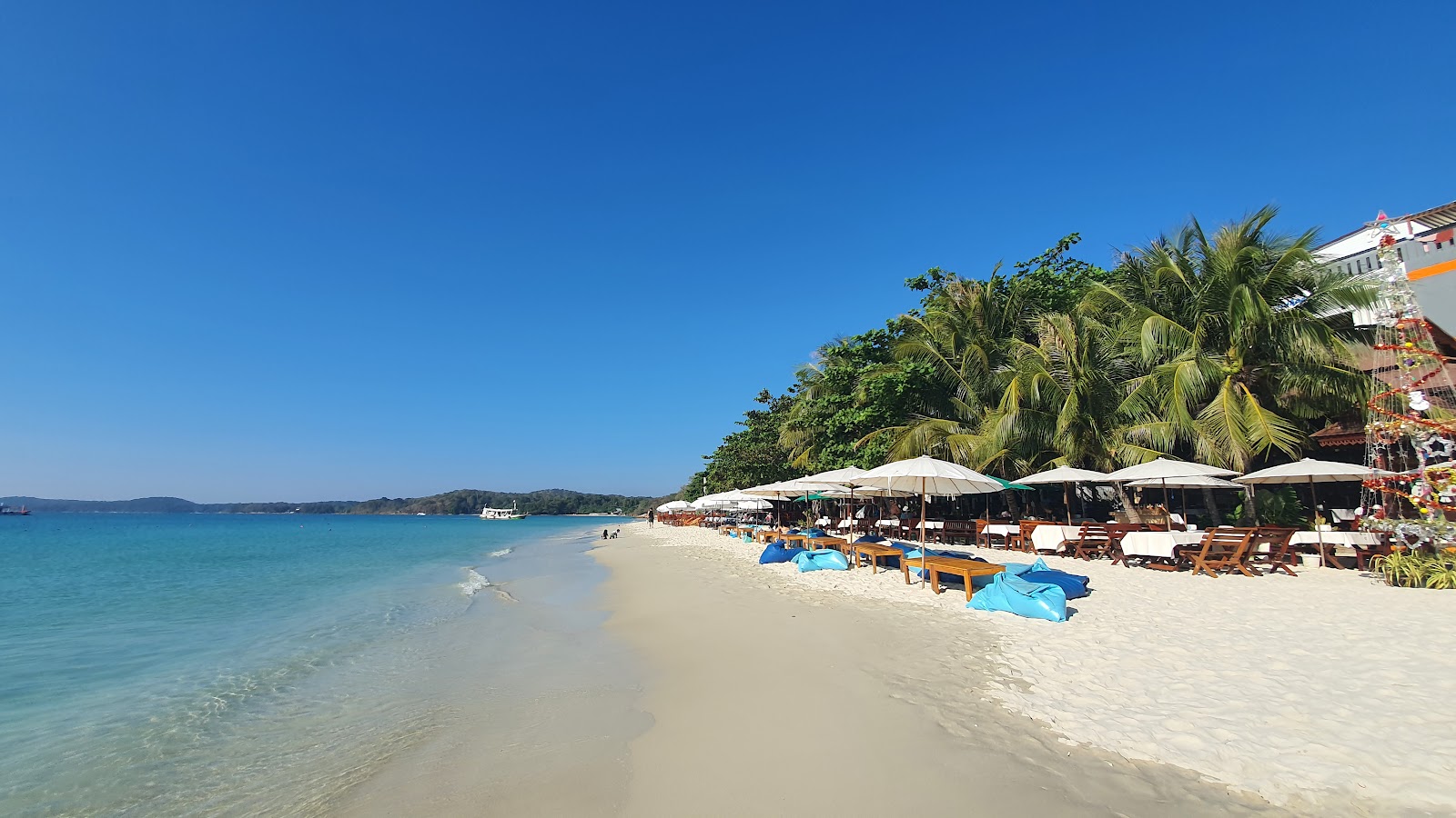 White sand and clear water along Sai Kaew Beach on Koh Samet, with beach umbrellas under palm trees