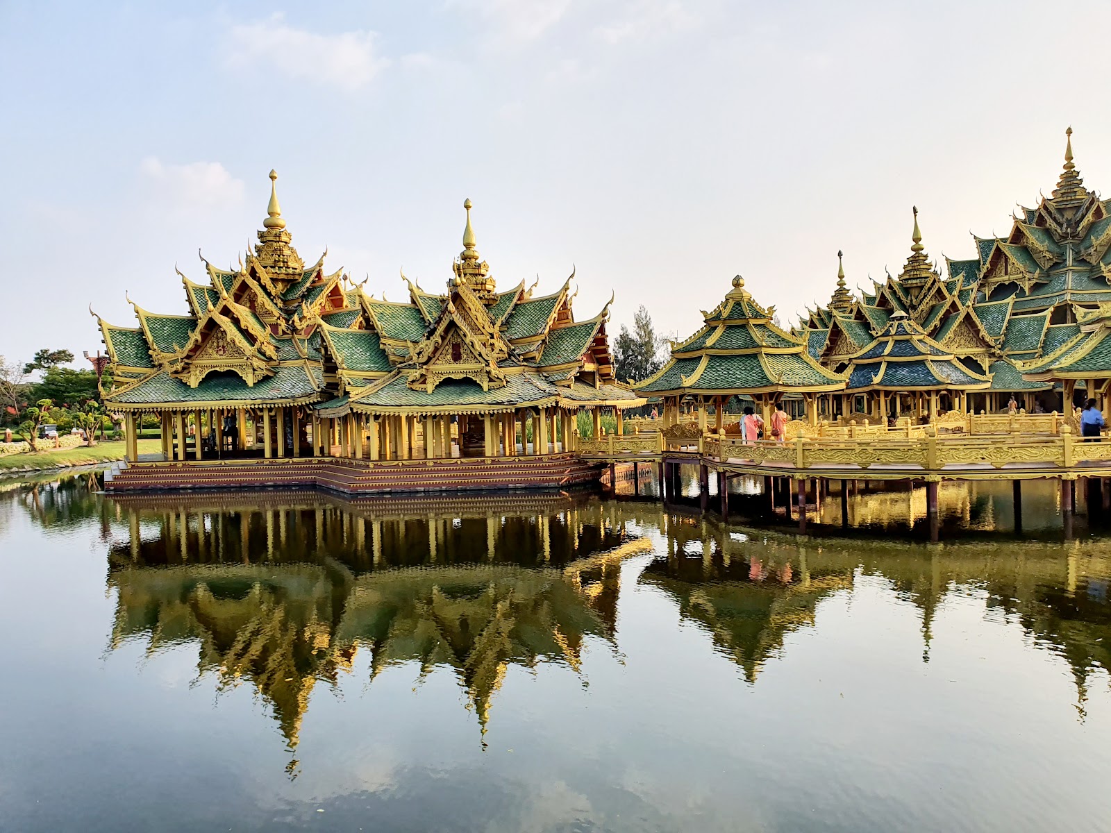 A gilded Thai pavilion with tiered roofs reflected in a lake at the Ancient City