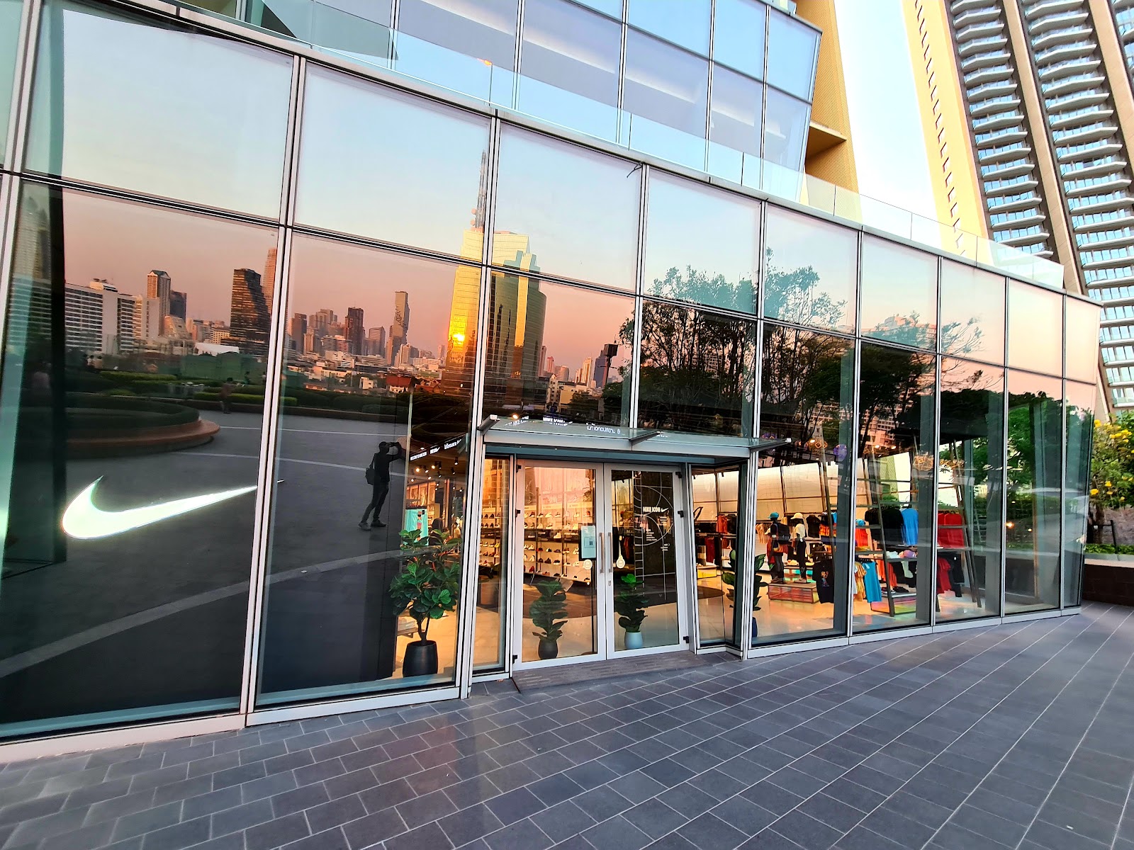 The Nike swoosh on the glass entrance of Nike ICONSIAM with the city skyline reflected at dusk