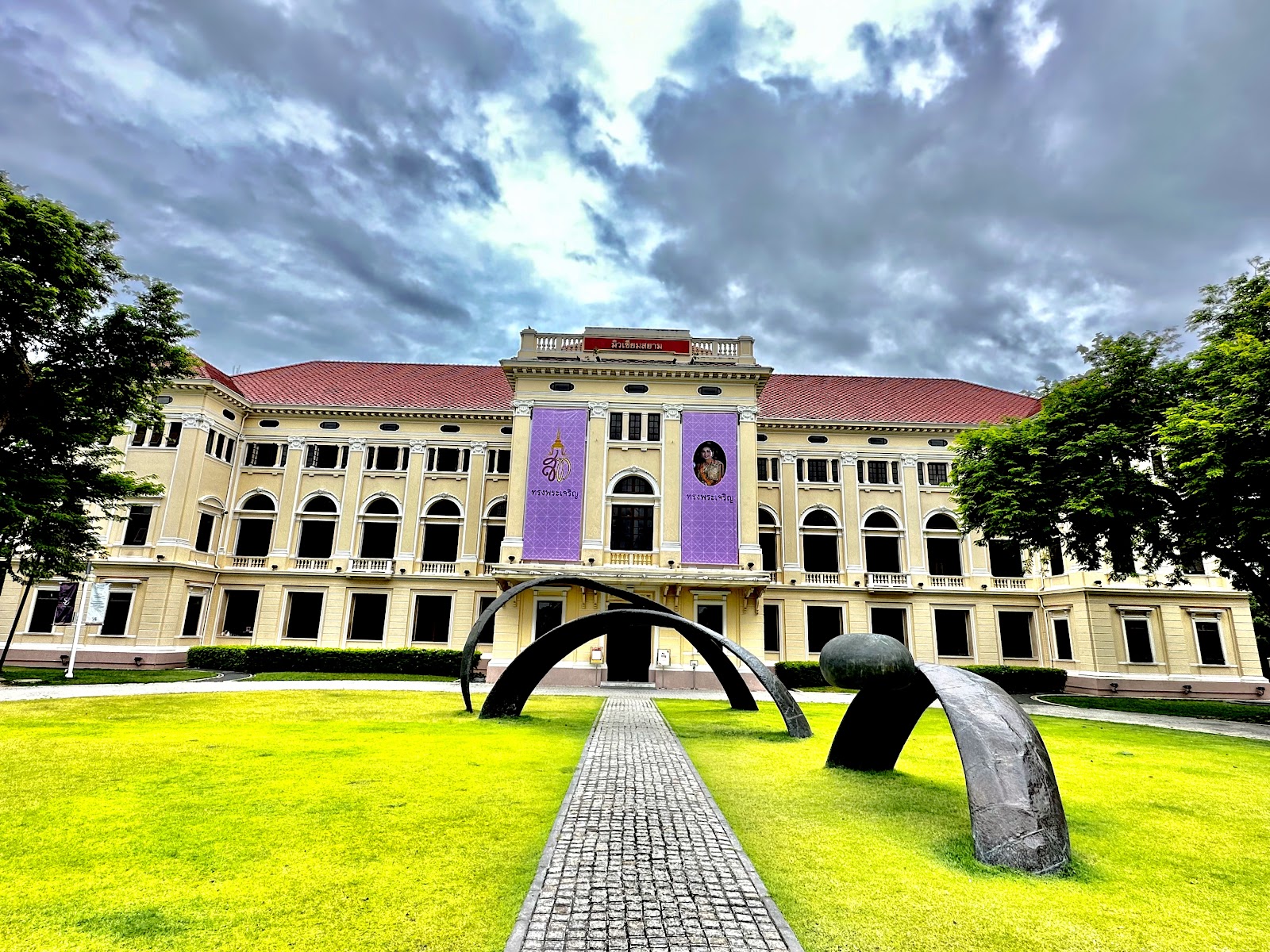 The yellow colonial-era facade of Museum Siam behind its lawn and arch sculptures