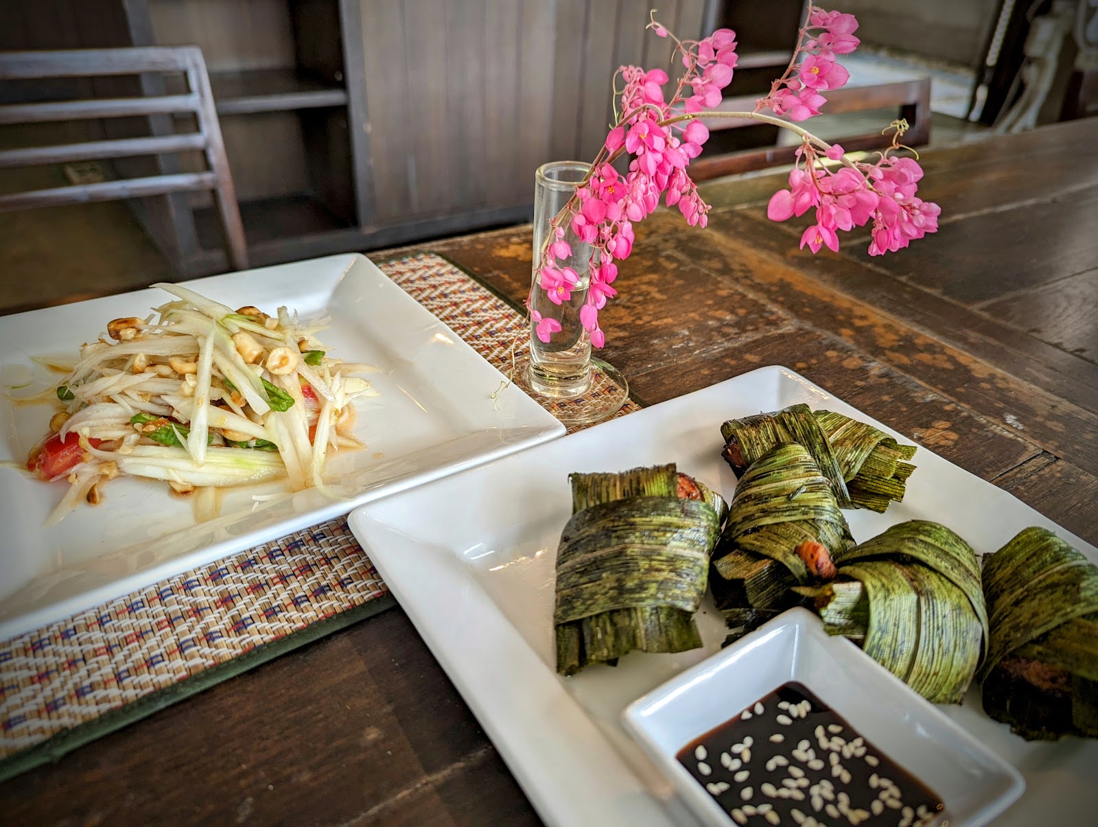 Green papaya salad and leaf-wrapped parcels with dipping sauce on a table at Baipai Thai Cooking School