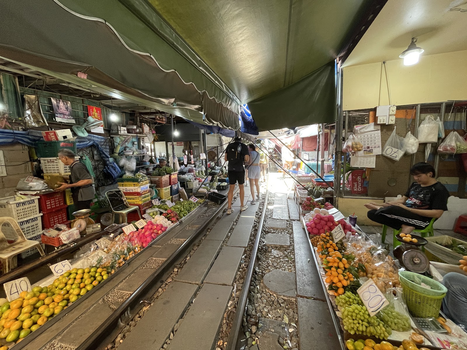 Fruit and vegetable stalls lining both sides of the railway track under awnings at the Maeklong Railway Market