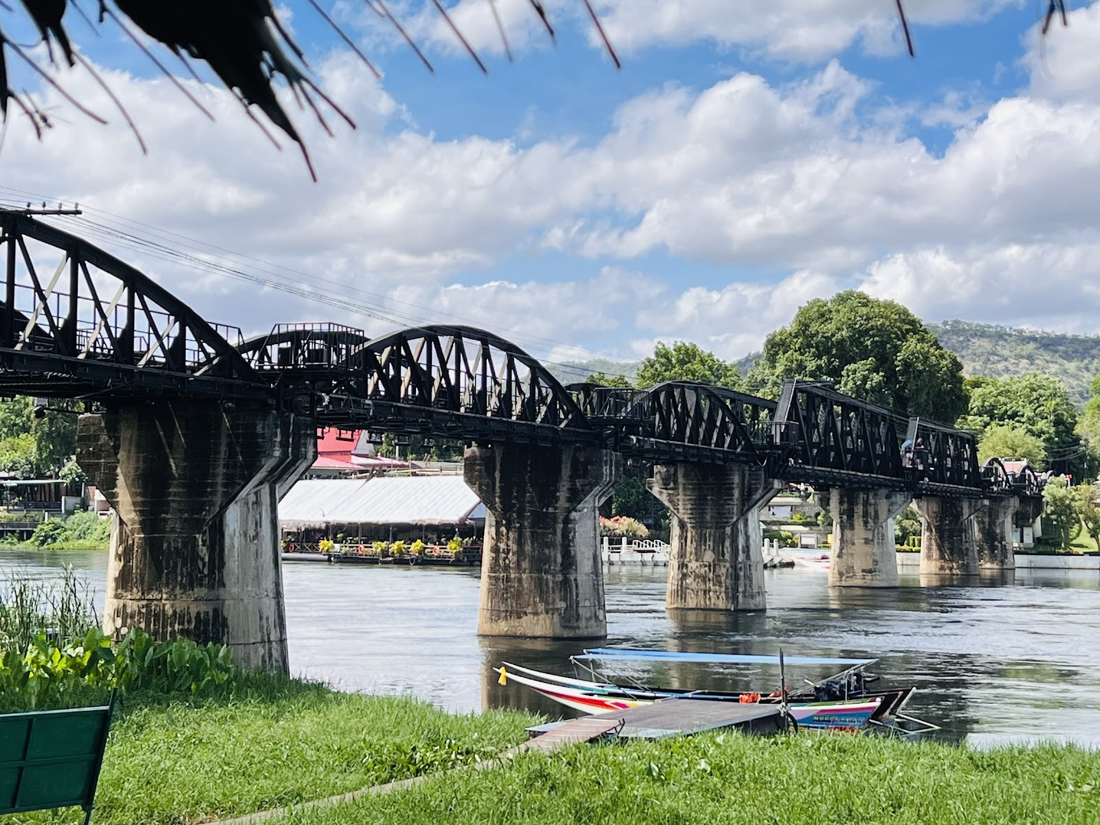 The black steel arched spans of the River Kwai bridge on concrete piers over the Khwae Yai River