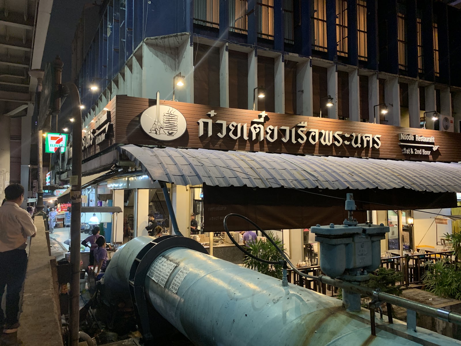 Boat noodle shopfronts with Thai signage along the canal bank at Boat Noodle Alley in the evening