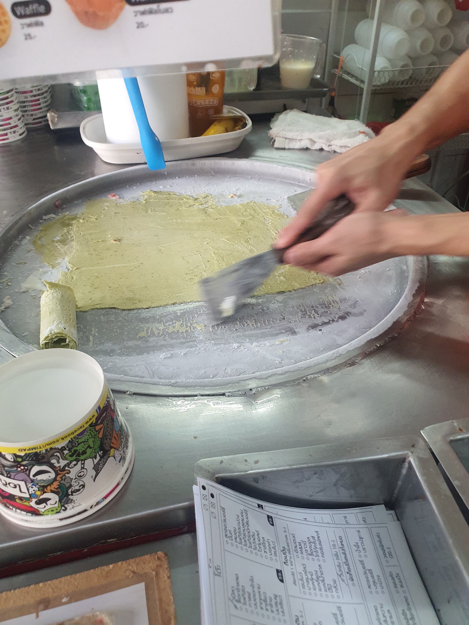 A scraper spreading ice cream on a round steel cold plate at Ice Manias Cafe