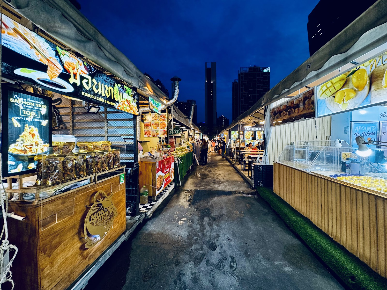 A lane of lit food stalls at Jodd Fairs night market at dusk