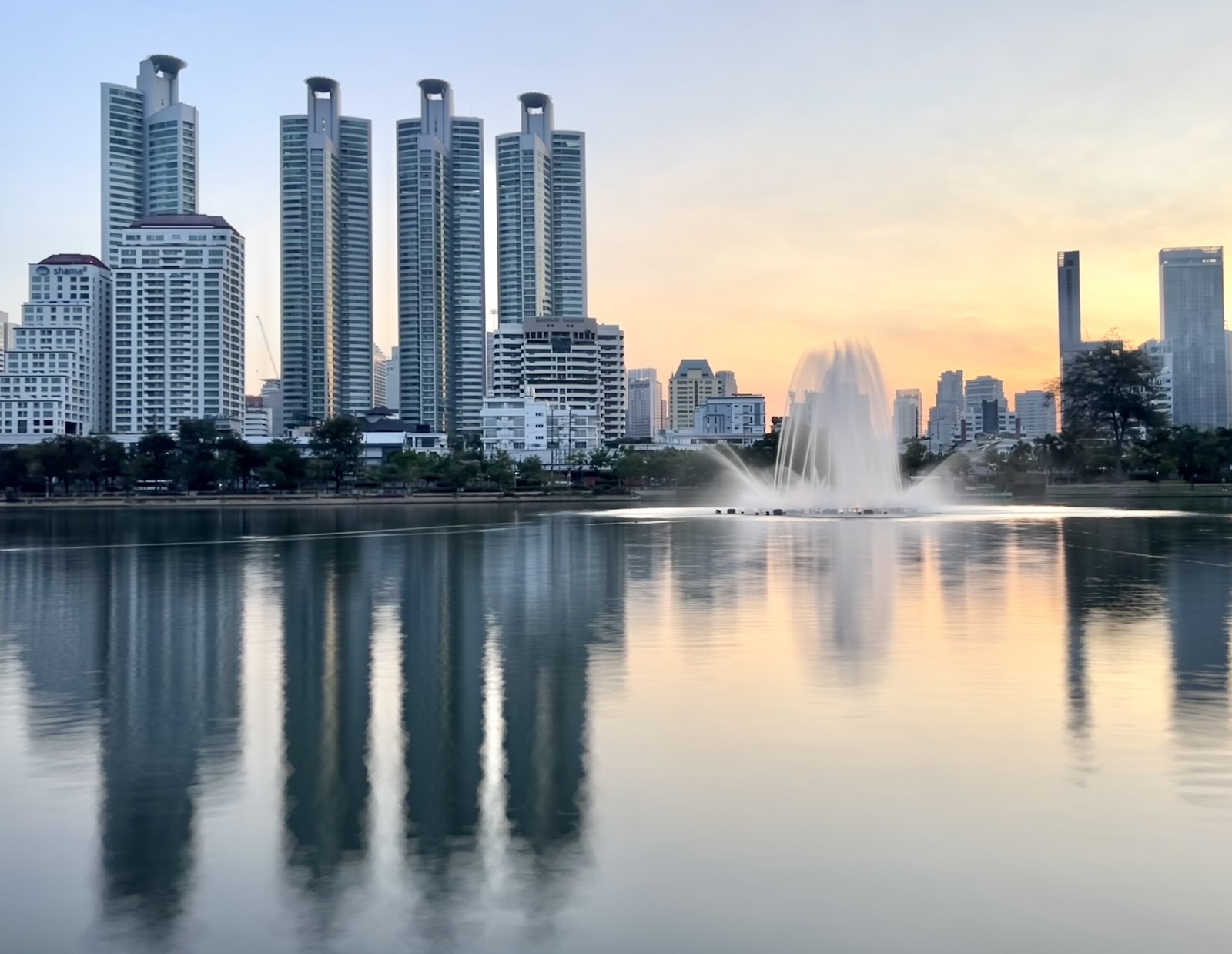 Residential and office towers reflected in the lake at Benjakitti Park at sunrise