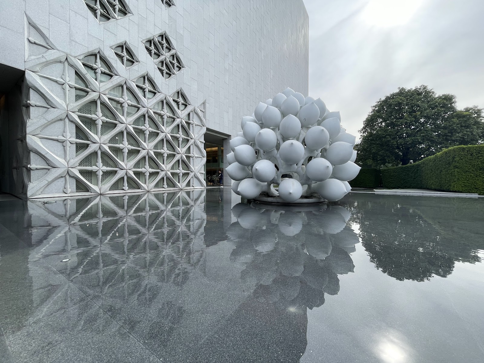 A white lotus sculpture in the reflecting pool beside the patterned facade of MOCA Bangkok