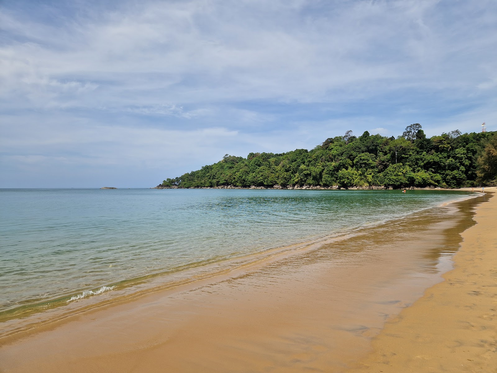 Calm water and a long sandy curve of Khao Lak Beach with a forested headland