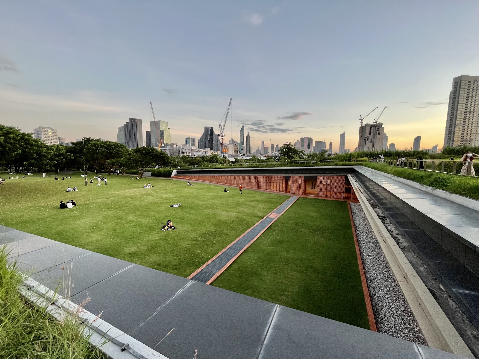 The sloping green roof lawn of Chulalongkorn University Centenary Park with Bangkok towers on the horizon