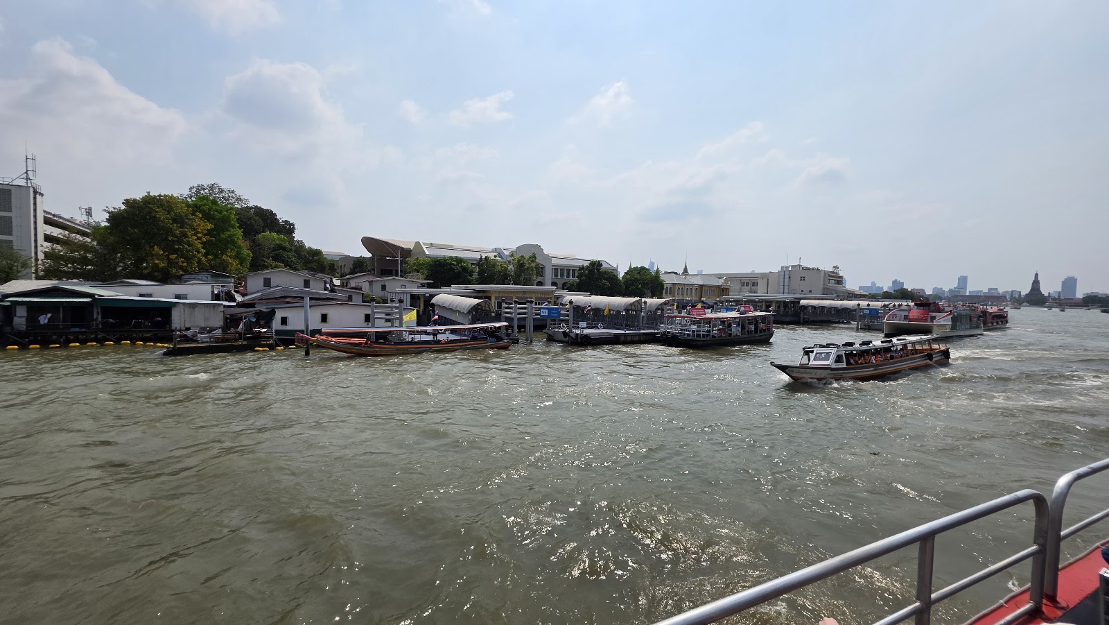 Low riverside buildings and a boat on the brown water of the Chao Phraya River