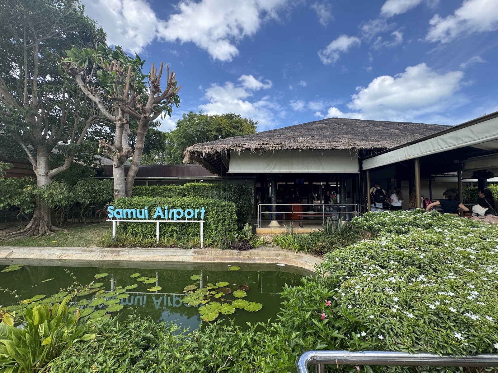 Thatched open-air terminal buildings and a lily pond beside the Samui Airport sign
