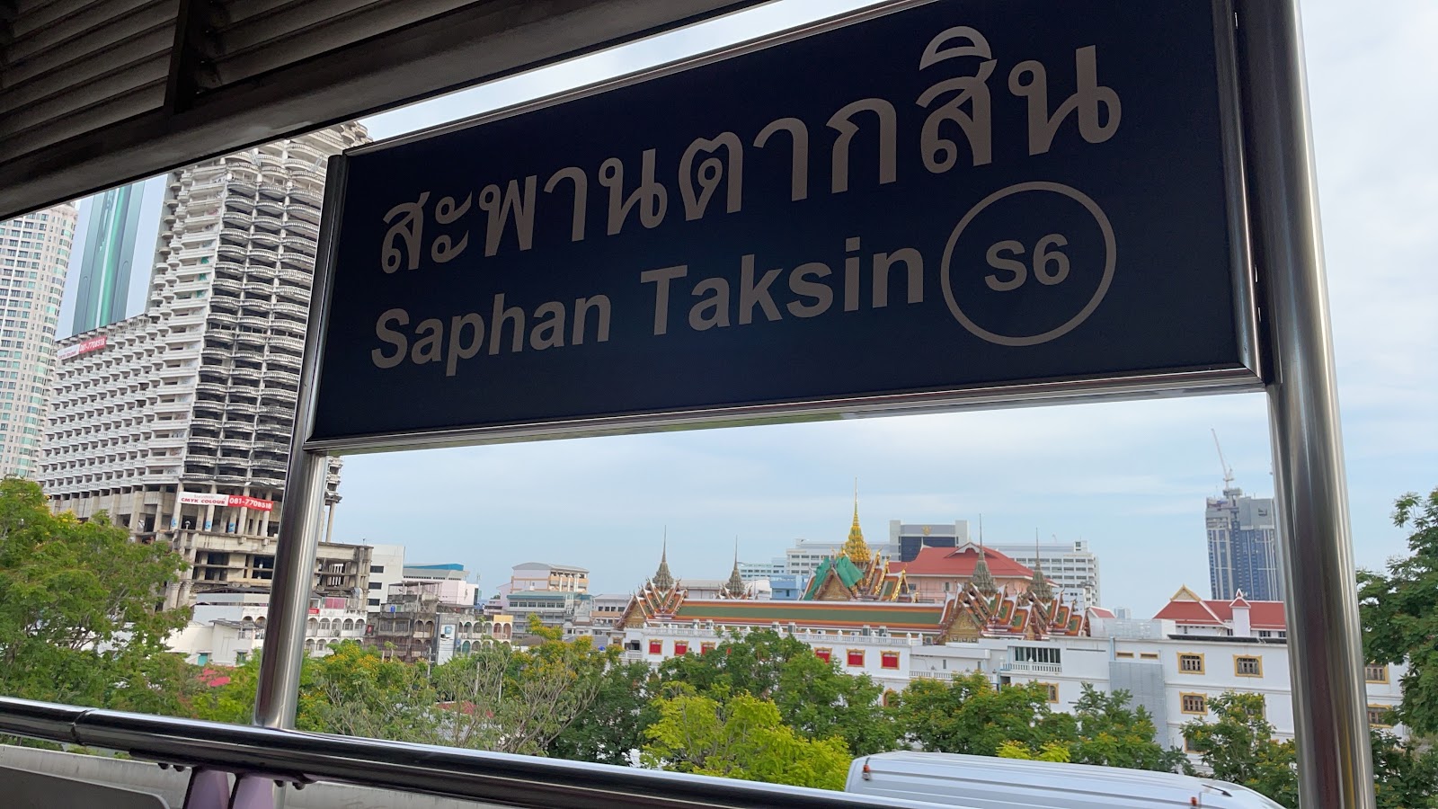 The Saphan Taksin S6 station sign on the BTS platform, with the Chao Phraya riverbank beyond