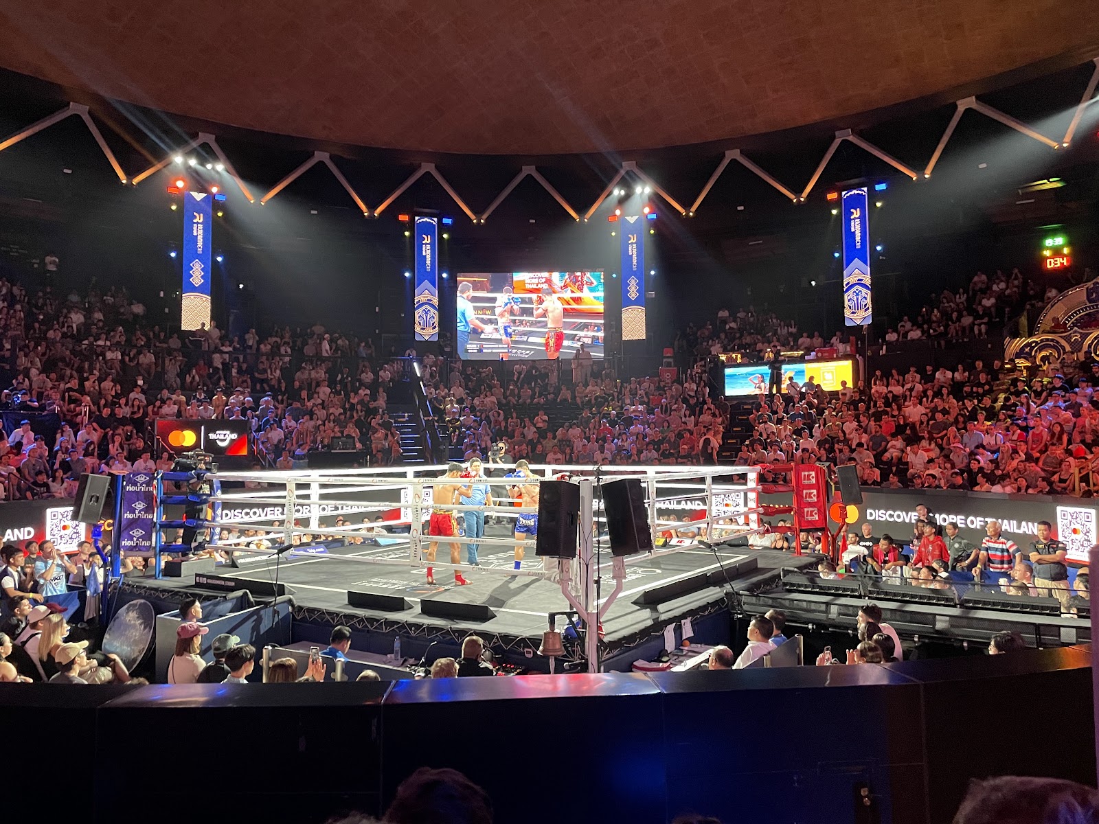 A Muay Thai bout in the ring at Rajadamnern Stadium with a full crowd and screens overhead