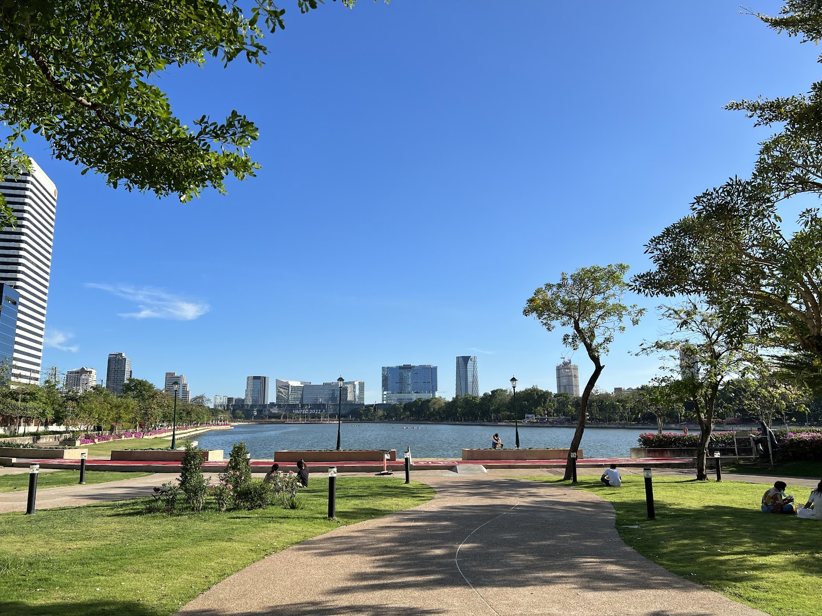 Paths and lawns beside the lake at Benjakitti Forest Park with city towers beyond