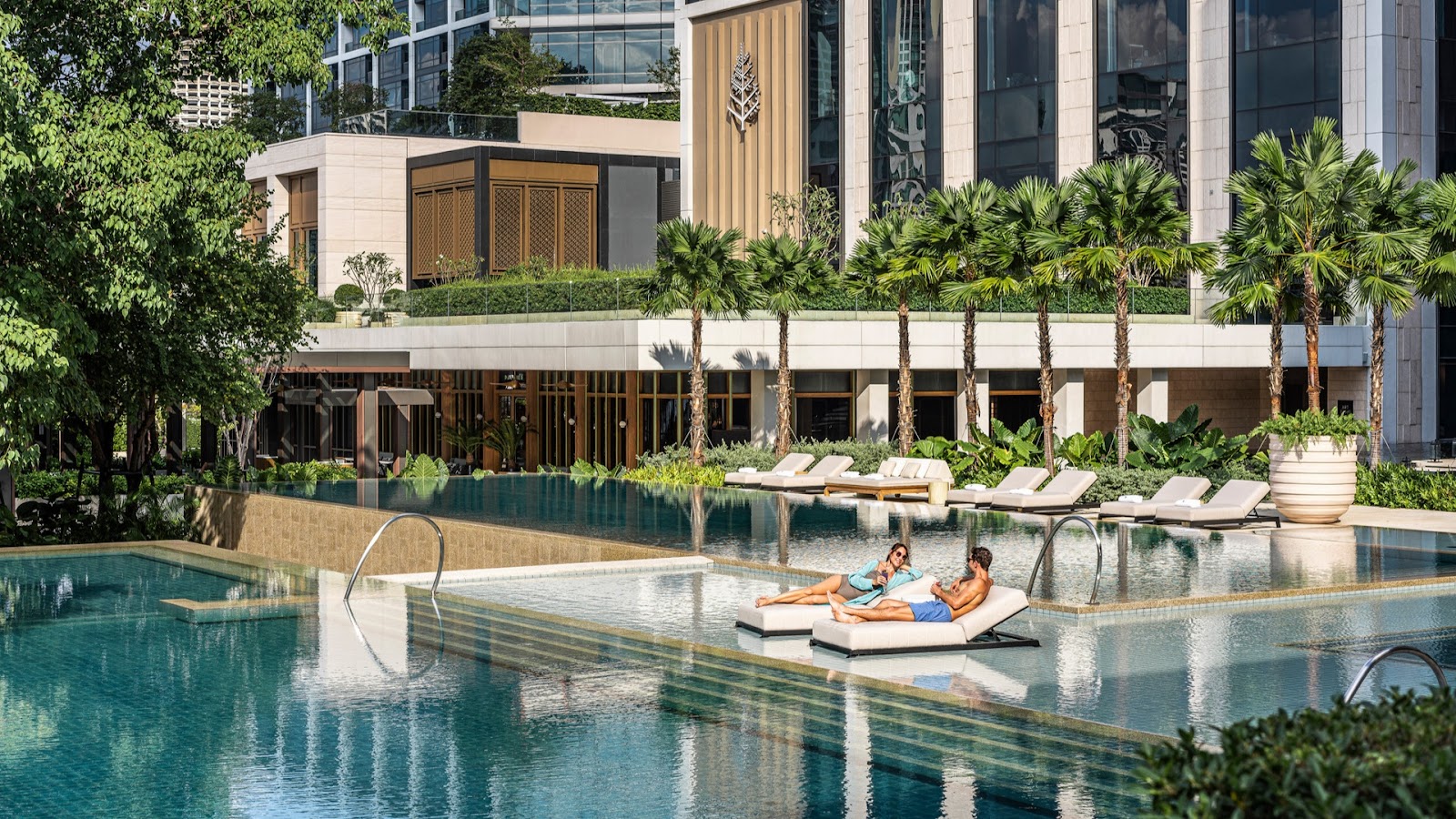 Four Seasons Hotel Bangkok's long riverside pool with sun loungers in front of the low-rise hotel buildings