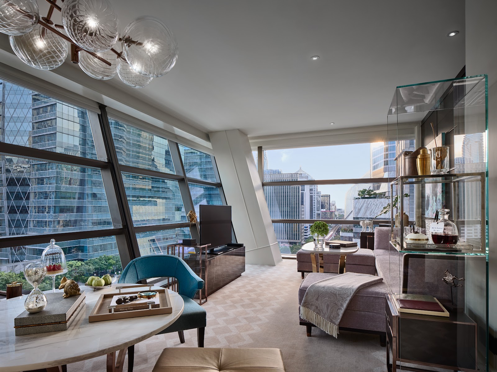 A corner suite living room with slanted floor-to-ceiling windows over office towers