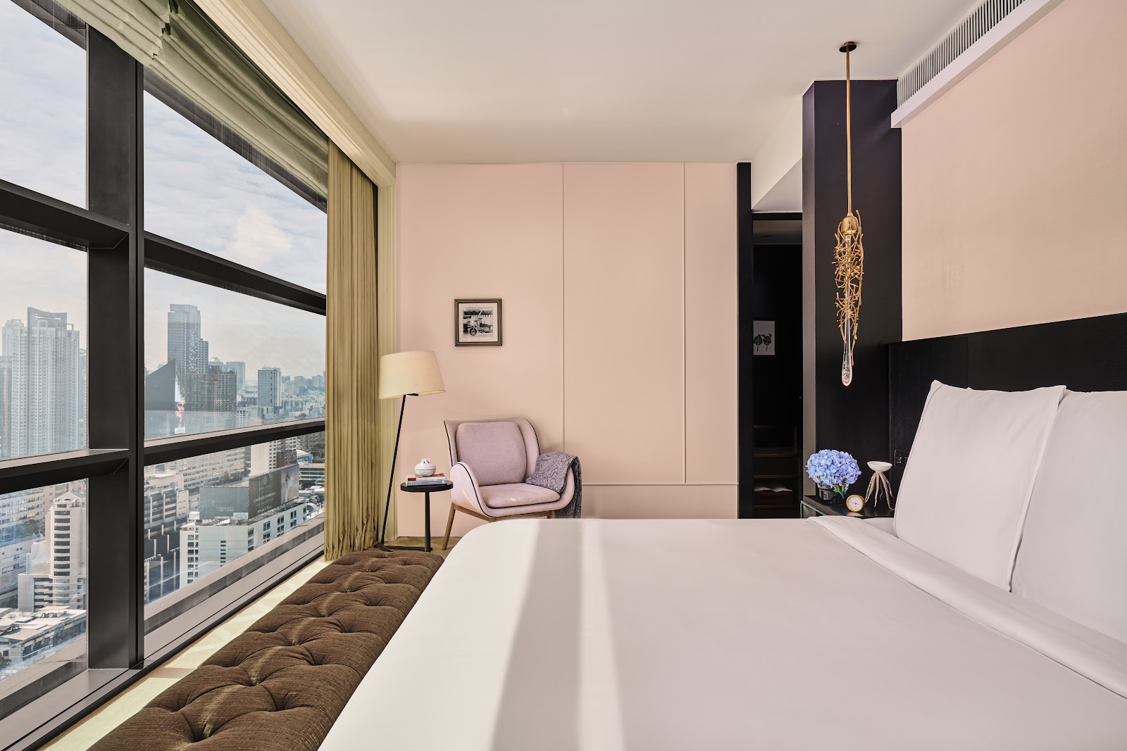 A guest room with a bed facing tall windows over the city