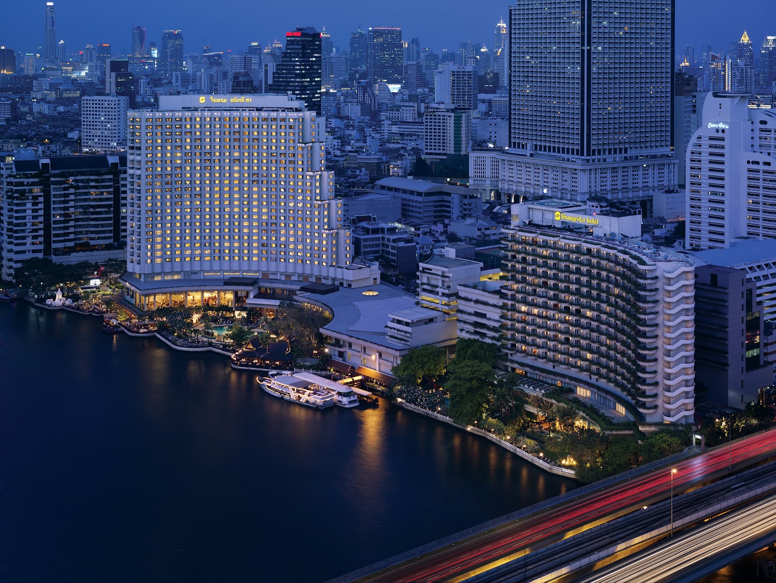 Shangri-La Bangkok's two towers on the Chao Phraya at dusk, with boats at the riverfront