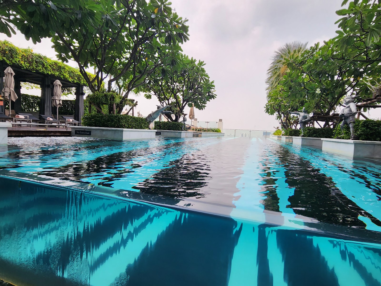 The St. Regis Bangkok's outdoor pool edge with frangipani trees and the city beyond