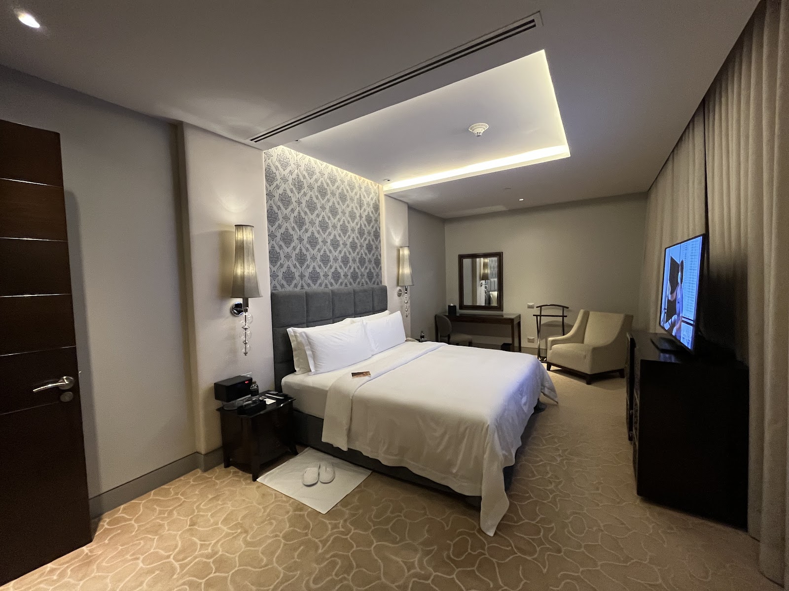 A St. Regis Bangkok guest room with a king bed, armchair and city window
