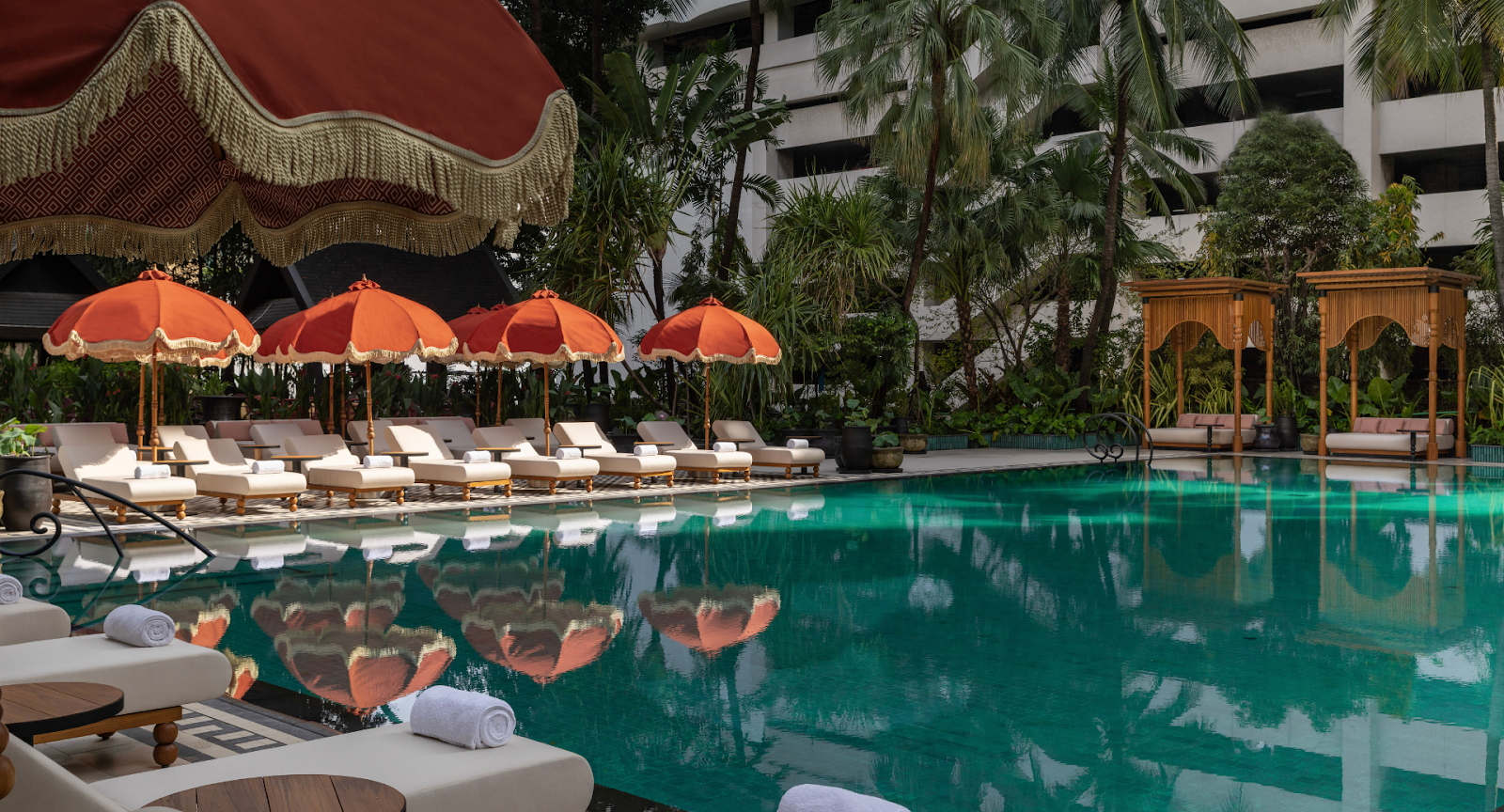 Anantara Siam Bangkok's garden pool with fringed parasols and loungers under palm trees