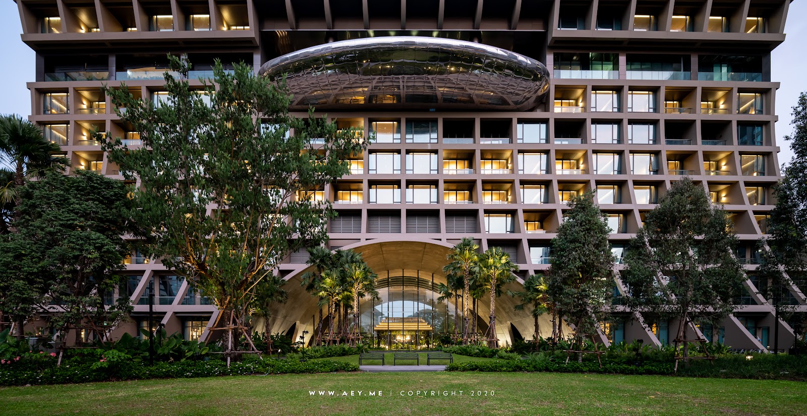 Sindhorn Kempinski's low, wide facade behind a lawn and mature trees at dusk