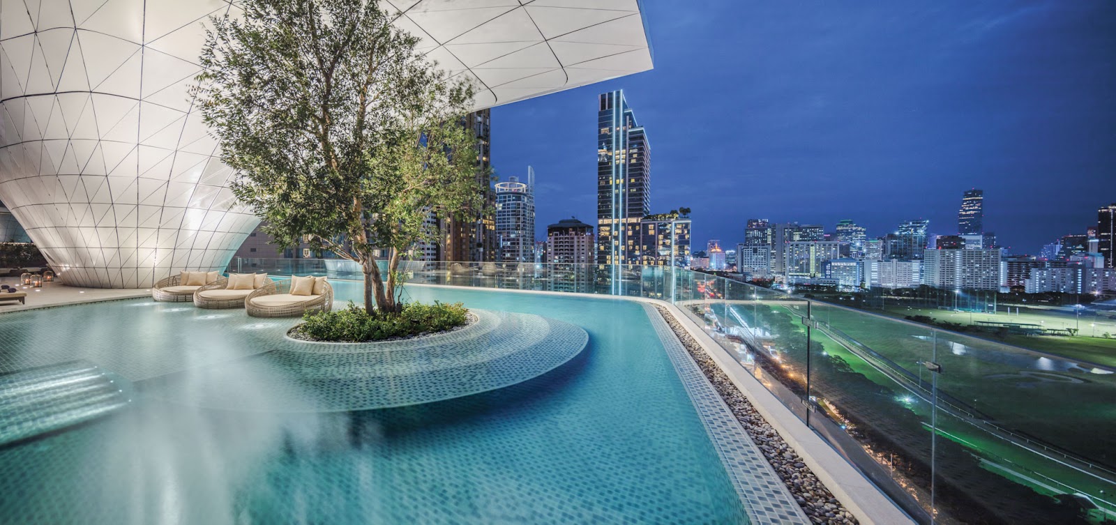 Waldorf Astoria Bangkok's infinity pool with a tree island and the city skyline at dusk