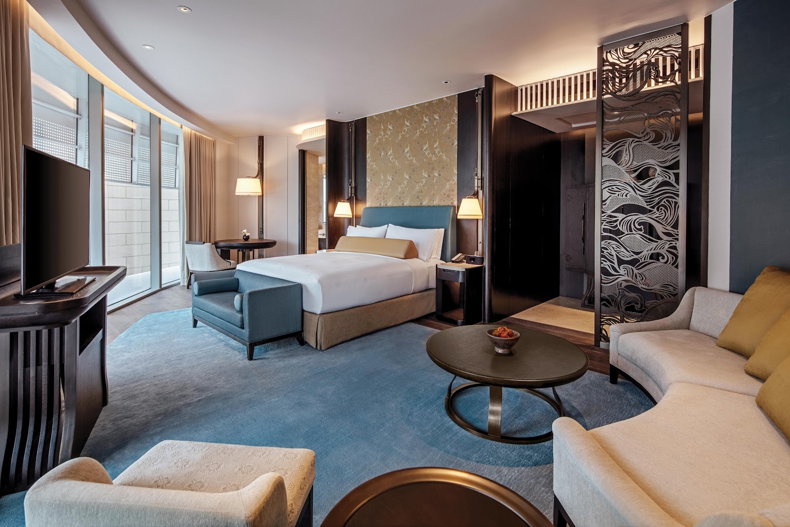 A Waldorf Astoria Bangkok room with a king bed, curved sofa and carved screen by the windows