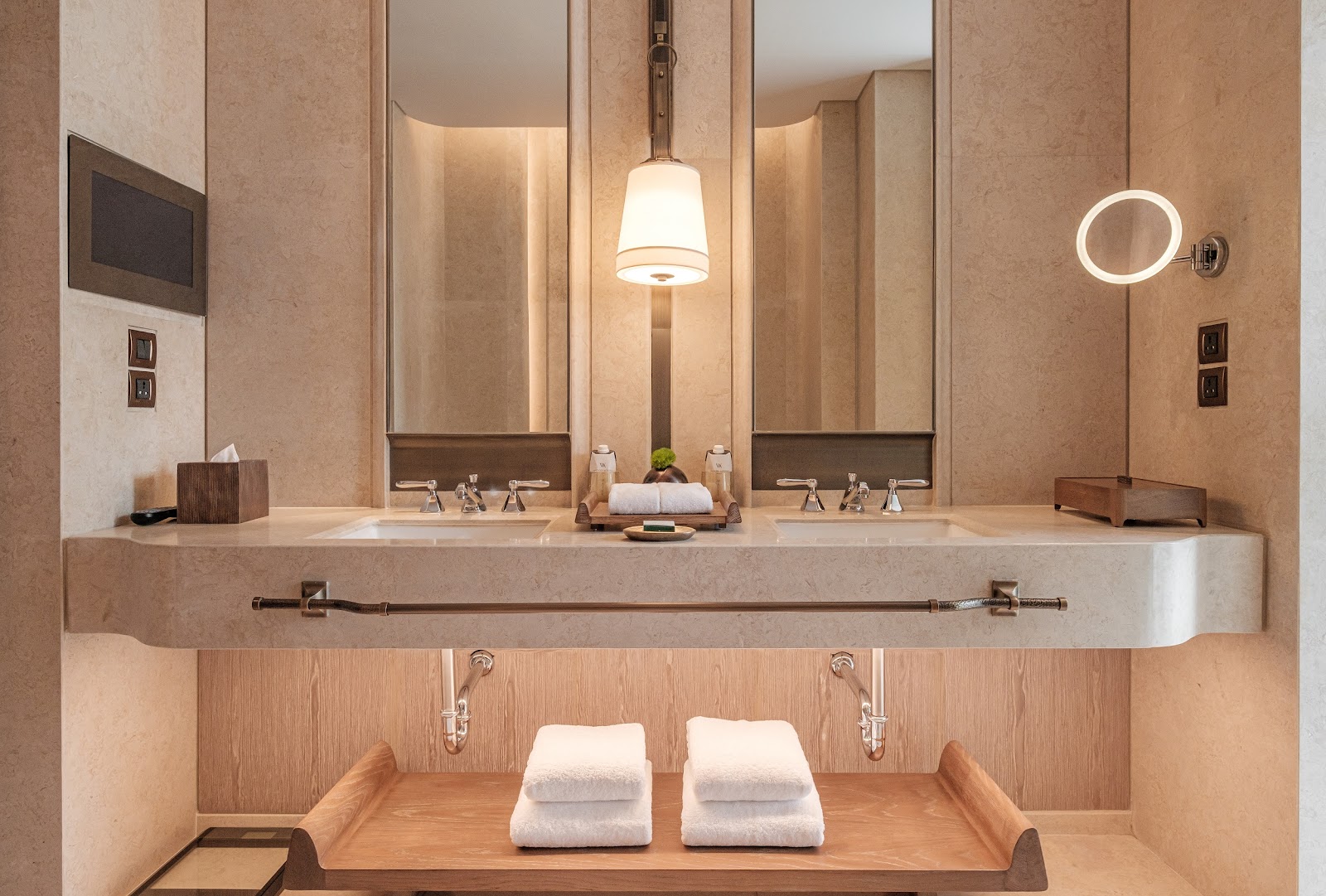 A marble bathroom with double vanities, round mirrors and warm lighting