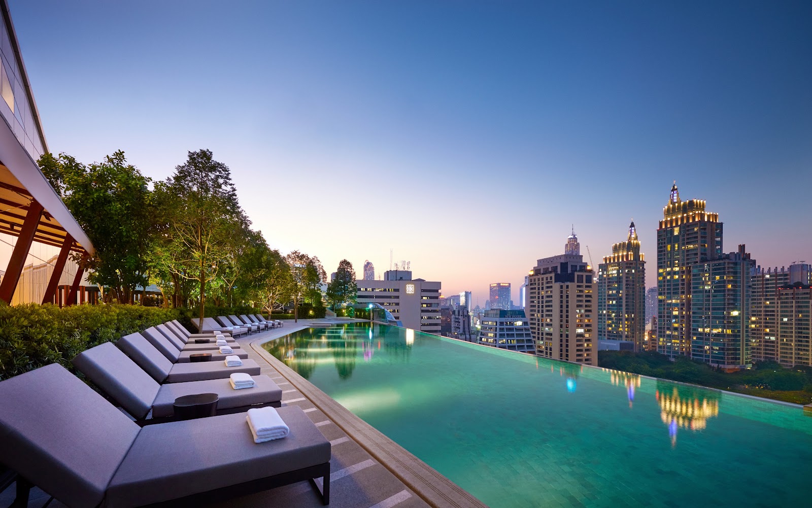 The infinity-edge pool of Park Hyatt Bangkok with loungers and the lit skyline at dusk