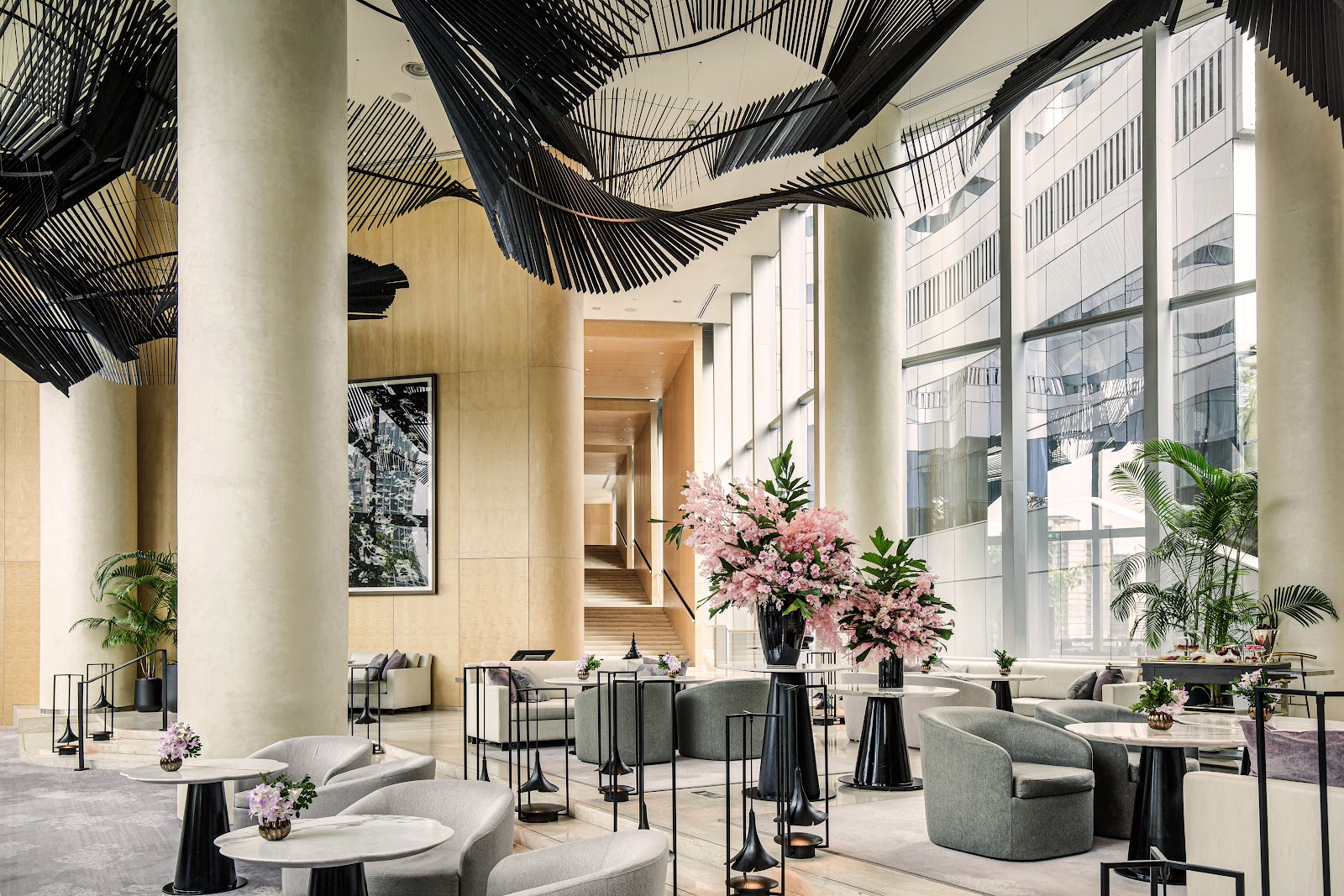Tall, light-filled lounge with armchairs, flowers and a large sculptural art installation overhead