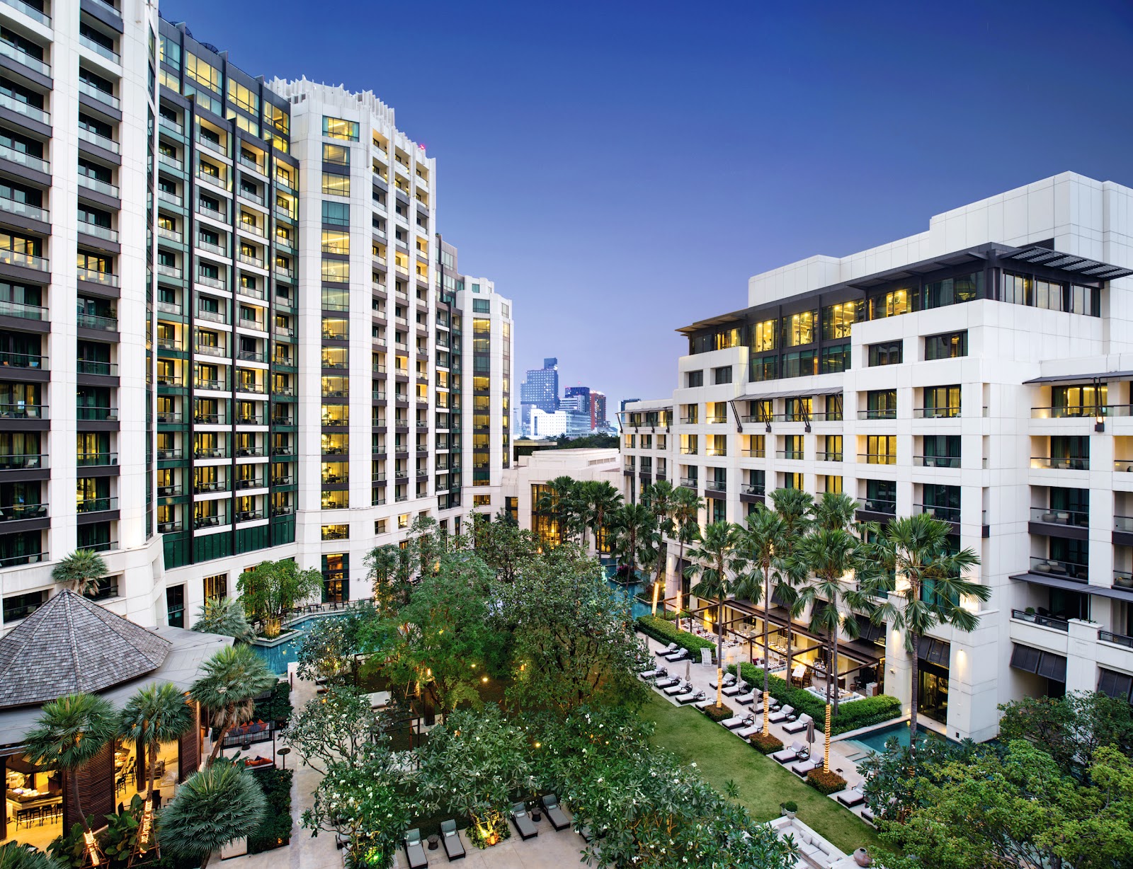 Aerial view of Siam Kempinski's hotel wings around tropical gardens and pools at dusk