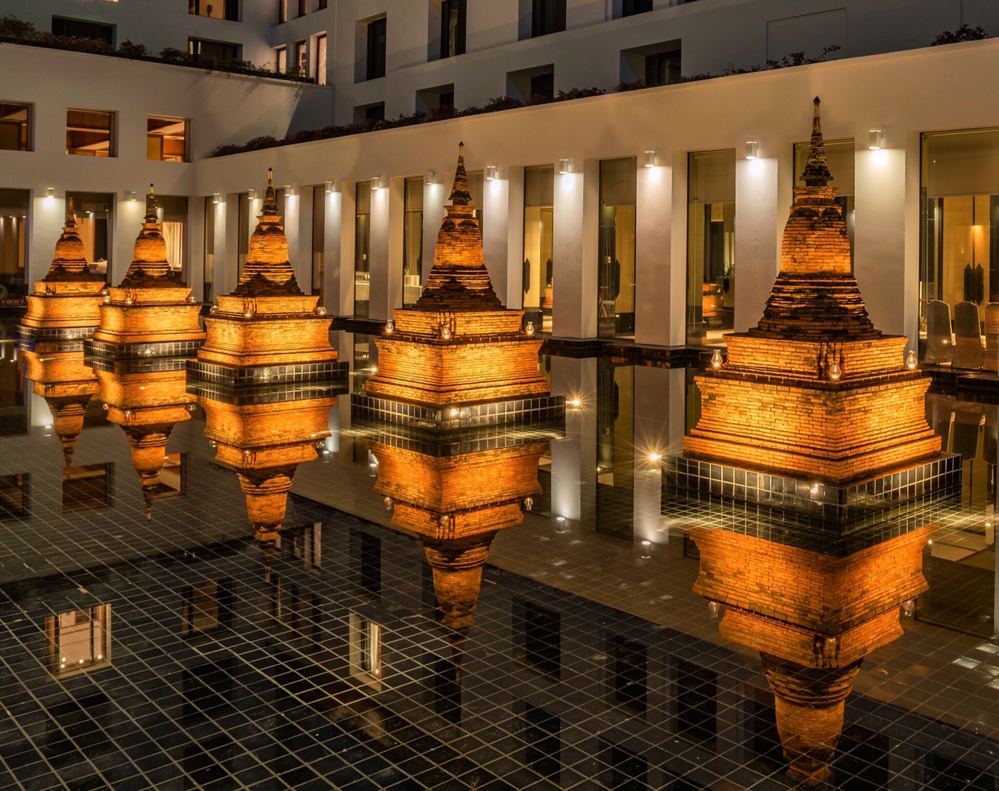 Brick chedis lit in gold at night, reflected in a dark pool between white colonnades