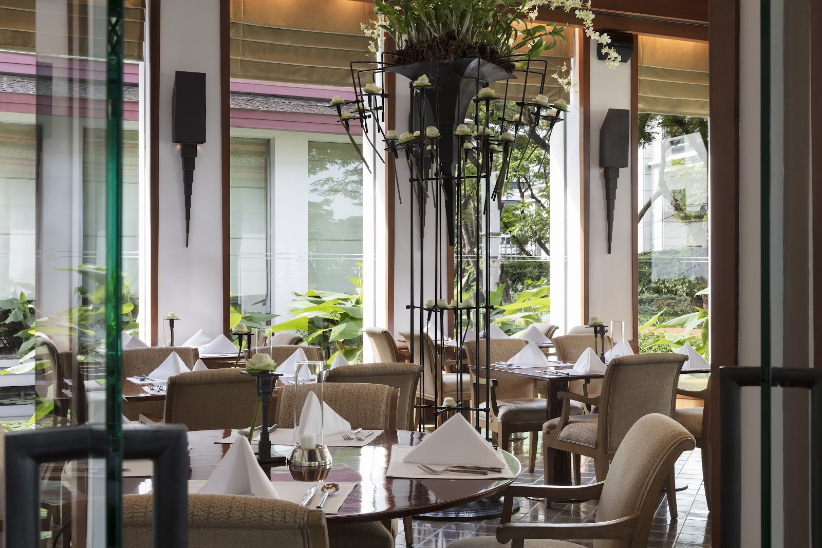 Dining room with set tables beside tall windows onto greenery