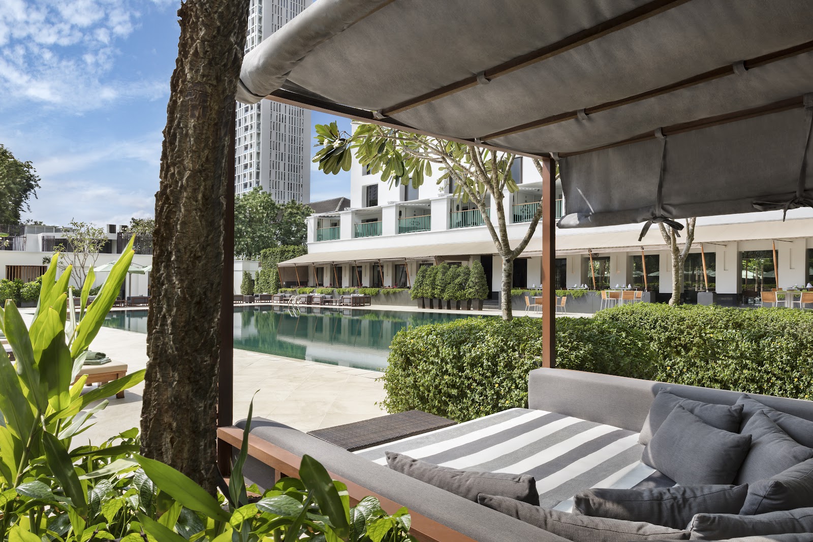 Shaded daybed beside the long outdoor pool framed by palms and plants