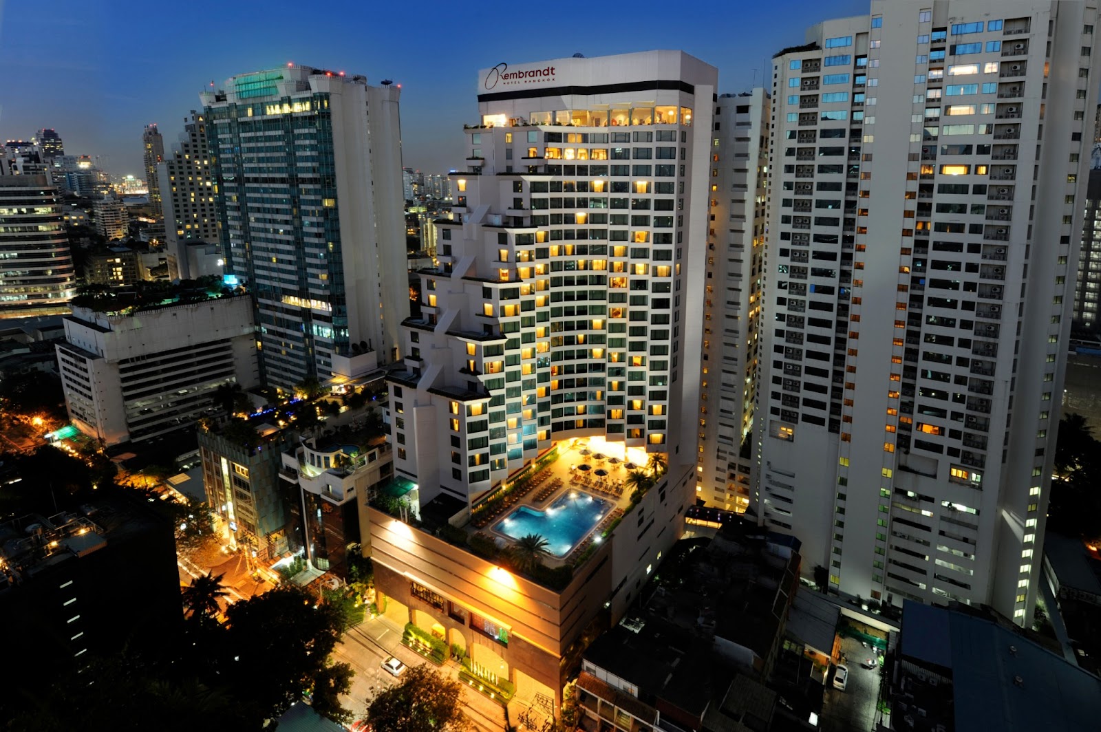 The Rembrandt Hotel tower lit at night among Sukhumvit high-rises, with the pool deck glowing below