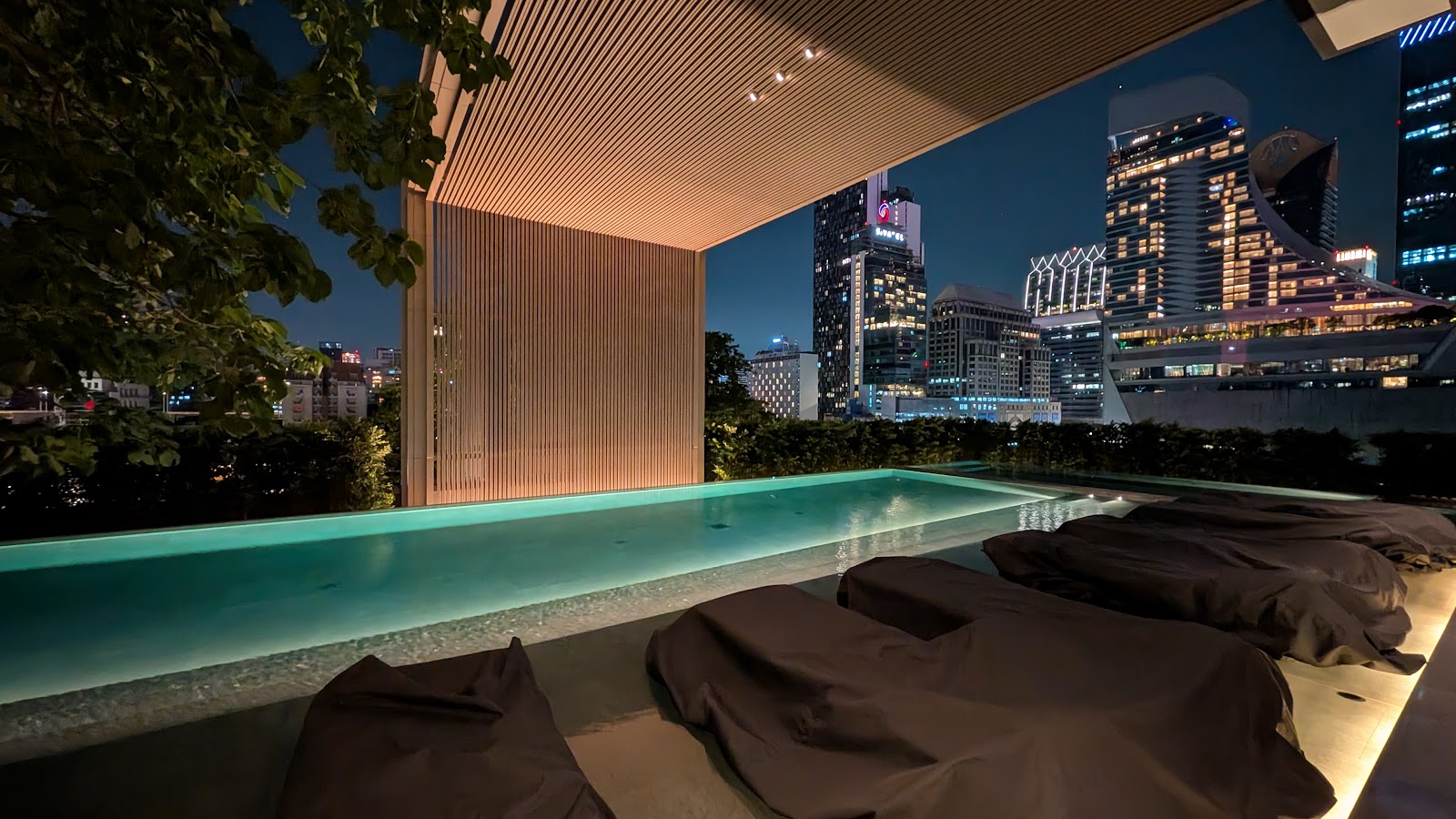 Long lit pool beside a covered terrace with the Bangkok skyline at night