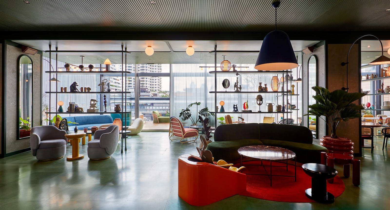 Lounge with colorful curved sofas, shelving and pendant lamps beside tall windows